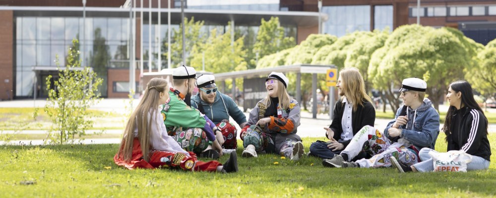 Opiskelijoita istuu LUT-yliopiston nurmikolla.
