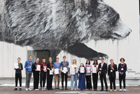 TuKoKen voittajat seisovat Otaniemen lukion seinässä olevan karhumuraalin edessä.