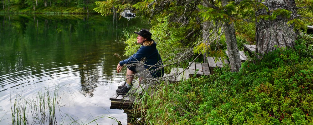 Henkilö istuu laiturilla järven rannalla. 