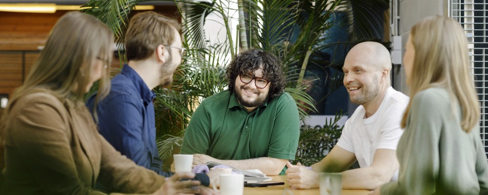 Kumpula kampus henkilöitä pöydän äärellä keskustelemassa