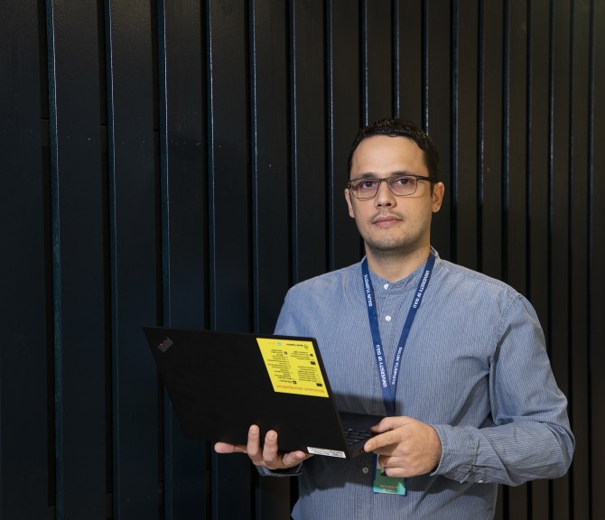 TEKin väitöskirjapalkittu, apulaisprofessori Onel Luis Alcazar López seisoo tummaa seinää vasten ja pitää kannettavaa tietokonetta kädessään.