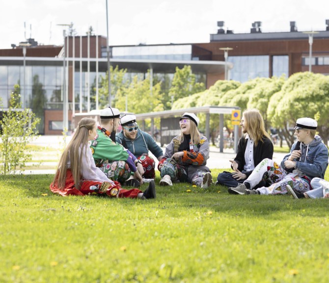 opiskelijoita istuu nurmikolla