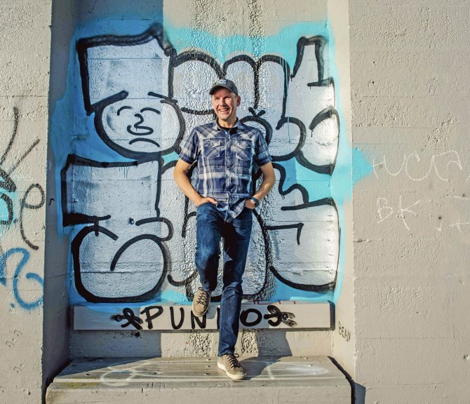 Matti Suokko nojailee betoniseinään, jossa on iso graffiti.