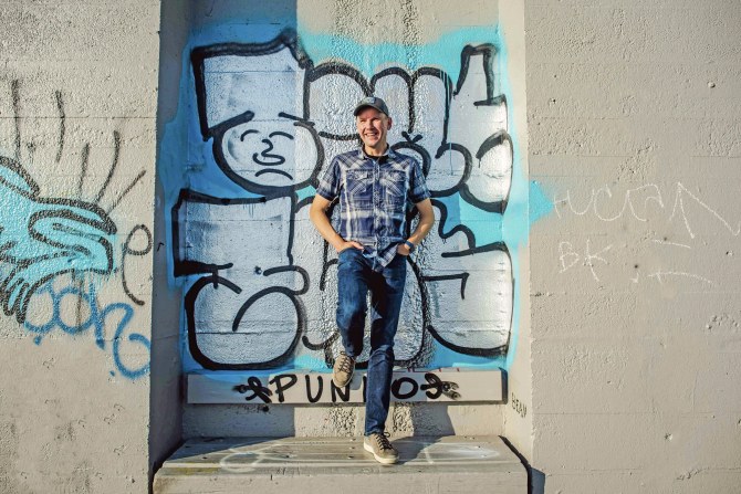 Matti Suokko nojailee betoniseinään, jossa on iso graffiti.