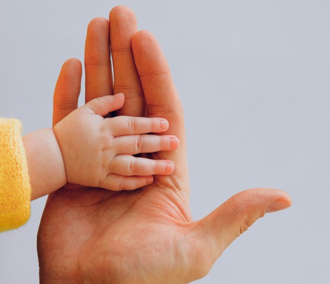 Two hands: one is an adult hand and the other a hand of a baby.