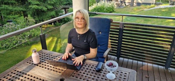 Aino Mensonen istuu terassilla tietokoneen ääressä, takana puutarha.