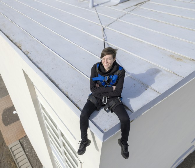 Mirika Knuutila istuu rakennuksen katolla turvavaljaissa.