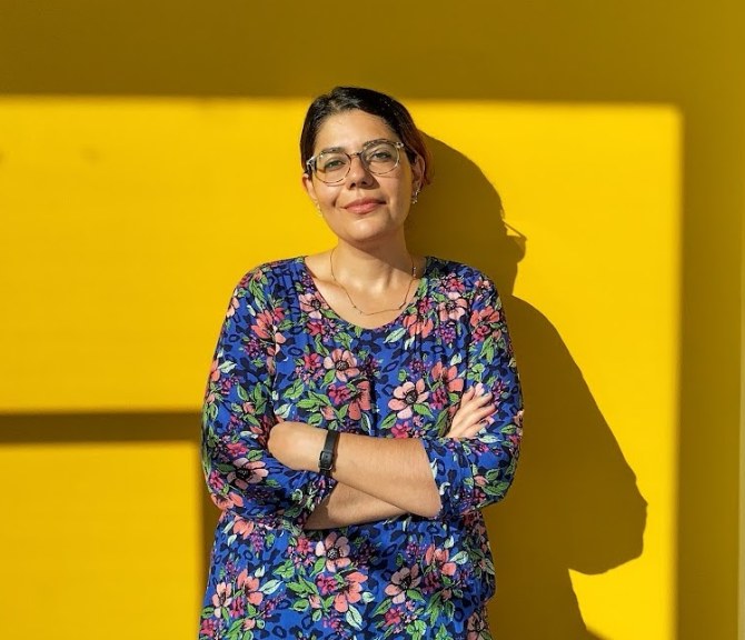 Negar Sharifi leaning on a sun-lit yeallow wall.