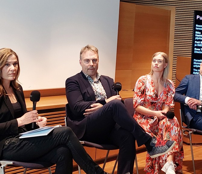 Panelistit istuvat yleisön edessä.