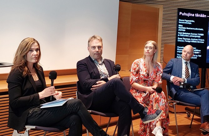 Panelistit istuvat yleisön edessä.