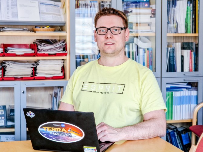 Tero Mielonen istuu kannettavan tietokoneen ääressä, takana on täysi kirjahylly.