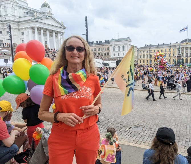 Sirkku Pohja seisoo Senaatintorin laidalla, kädessään TEKin sateenkaaren värinen lippu.