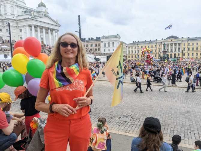 Sirkku Pohja seisoo Senaatintorin laidalla, kädessään TEKin sateenkaaren värinen lippu.