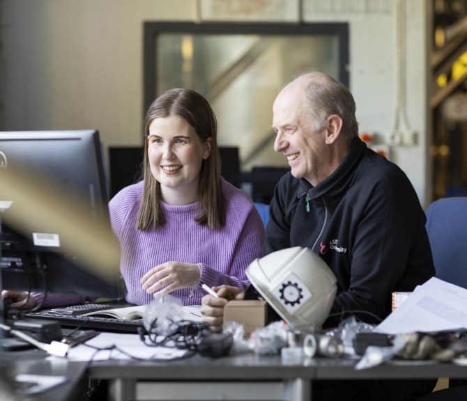 Kaksi henkilöä katsoo läppäriä työpöydän ääressä.