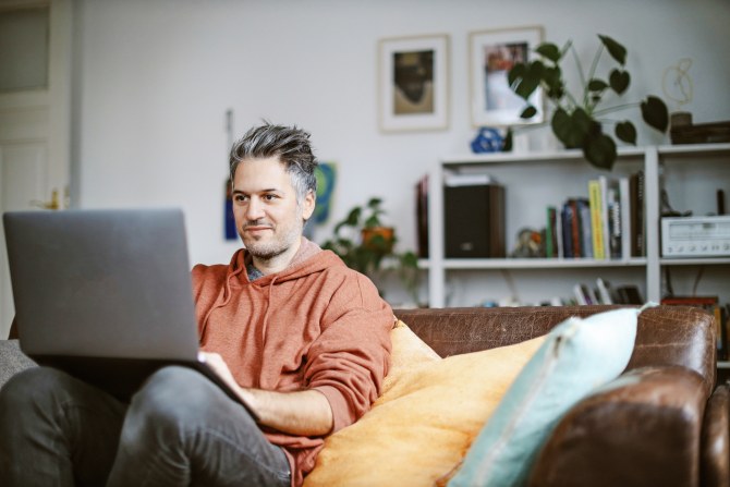 Mies istuu rennosti sohvalla tietokone sylissään