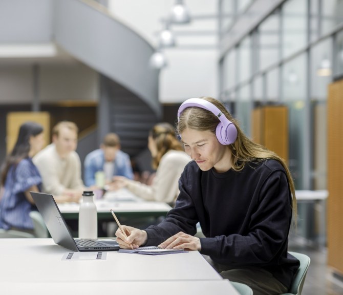 Opiskelija täyttää kalenteriaan kuulokkeet päässään.