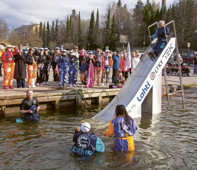Ihmisiä kerääntyneenä katsomaan, kun opiskelijat laskevat liukumäellä veteen.