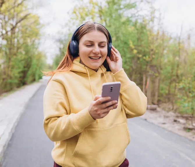 nainen, keltainen huppari, kännykkä, kuulokkeet