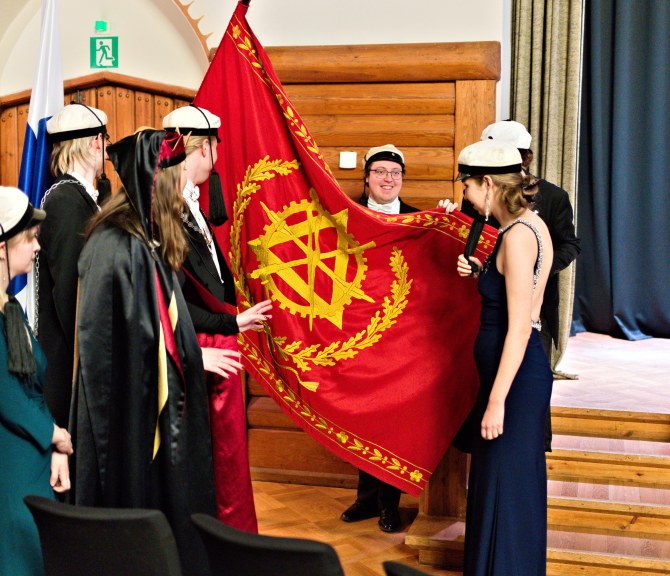 Juhla-asuisia ihmisiä teekkarilakit päässään lipun ympärillä.