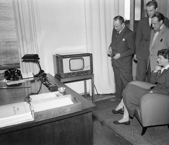 Mustavalkoinen kuva televisiosta ja ihmisistä katsomassa sitä.