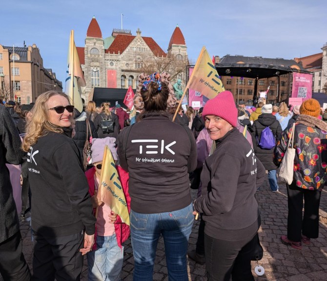 TEKin edustajat seisovat Rautatientorilla, jossa on paljon ihmisiä.