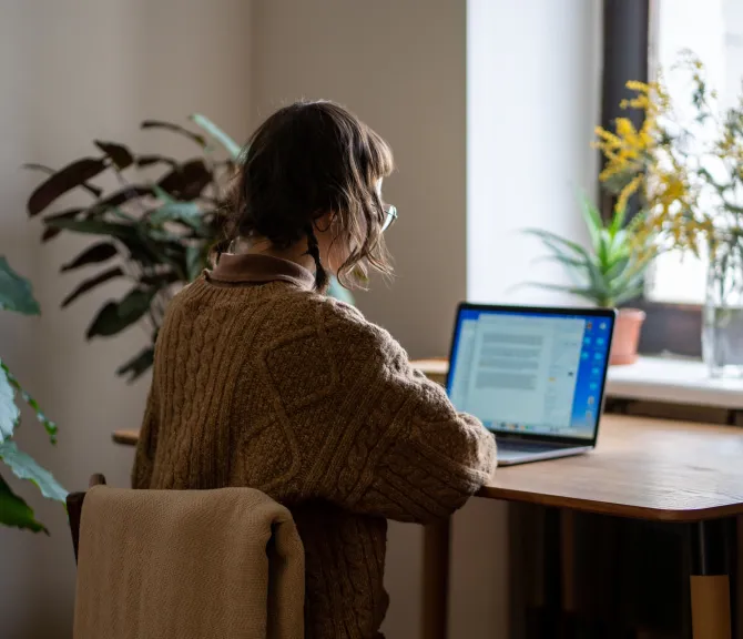 Nuorehko neisoletettu istuu tietokoneen ääressä kotonaan.