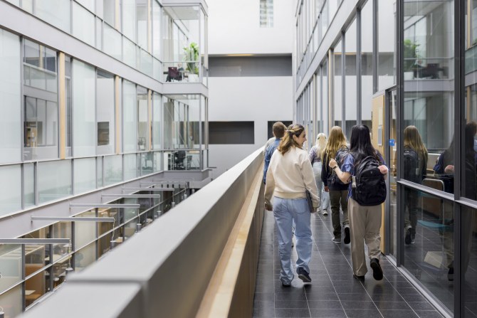 Ihmisiä kävelemässä käytävällä modernissa lasiseinäisessä toimistotilassa