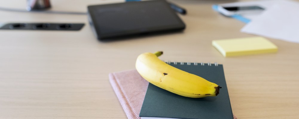 Työpöytä jossa vihkoja, kyniä, kirjoja sekä banaani