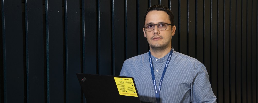 TEKin väitöskirjapalkittu, apulaisprofessori Onel Luis Alcazar López seisoo tummaa seinää vasten ja pitää kannettavaa tietokonetta kädessään.