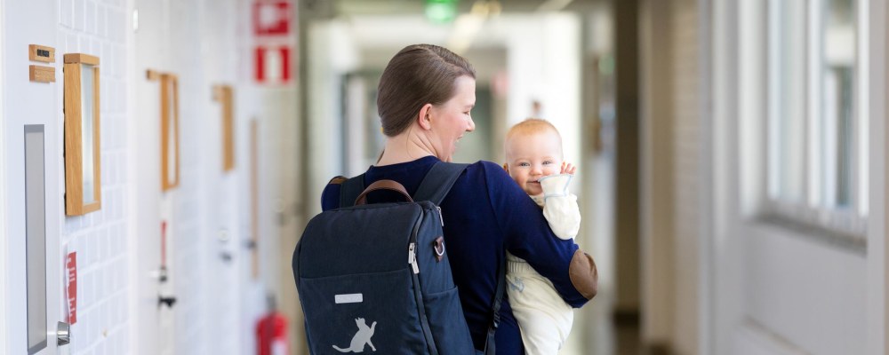 Nainen reppu selässään pitää sylissään pientä lasta, joka vilkuttaa kuvaajalle