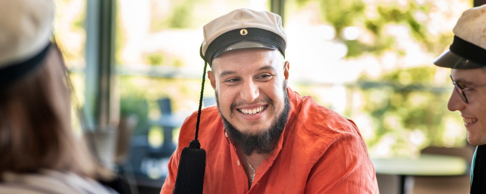 Henkilö istuu teekkarilakki päässään pöydän ääressä.