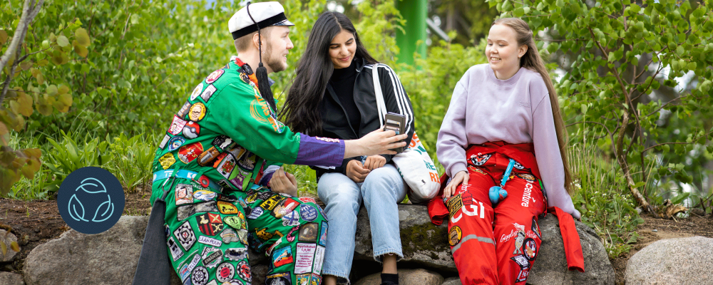 Opiskelijat istuvat ulkona, takanaan aurinkopaneeli.