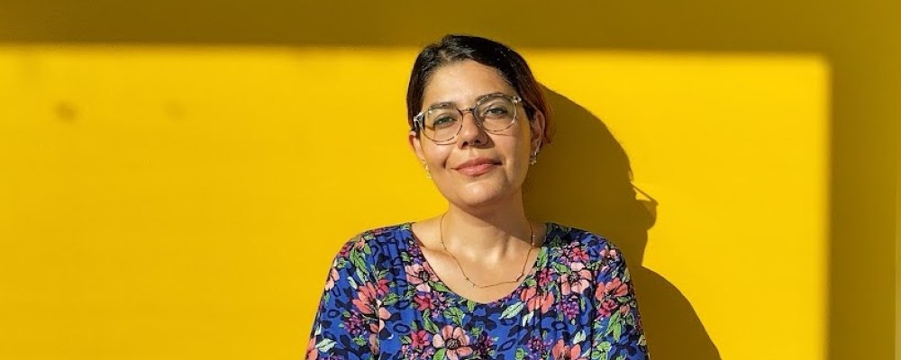 Negar Sharifi leaning on a sun-lit yeallow wall.