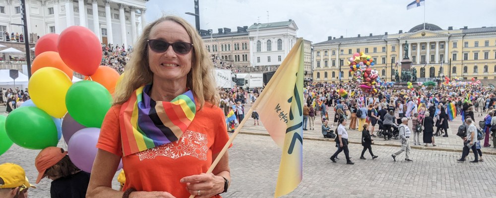 Sirkku Pohja seisoo Senaatintorin laidalla, kädessään TEKin sateenkaaren värinen lippu.