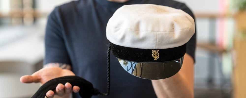 Henkilö pitää teekkarilakkia toisessa kädessään ja sen tupsua toisessa.