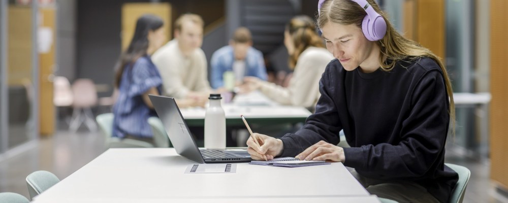 Opiskelija täyttää kalenteriaan kuulokkeet päässään.