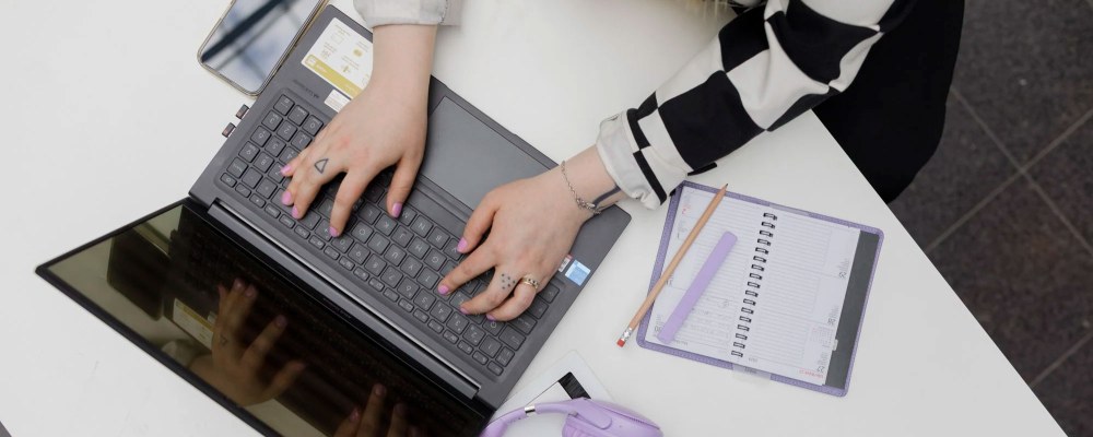 Ylhäältä päin otettu kuva henkilöstä, joka käyttää kannettavaa tietokonetta.