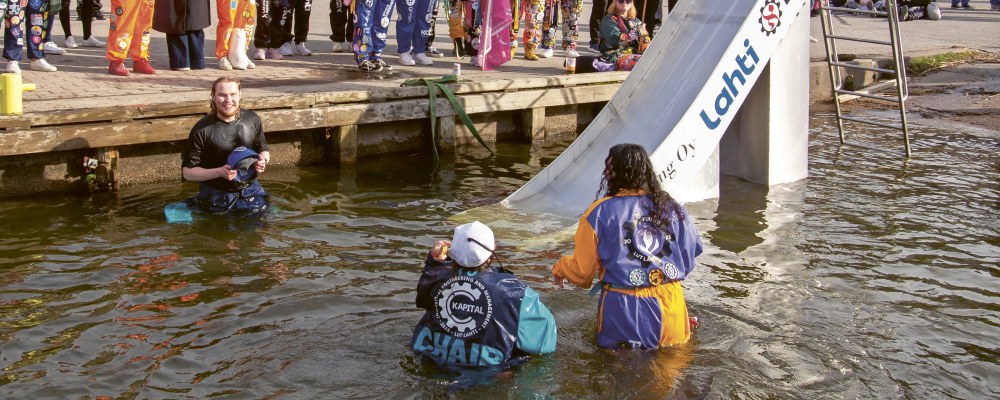 Ihmisiä kerääntyneenä katsomaan, kun opiskelijat laskevat liukumäellä veteen.