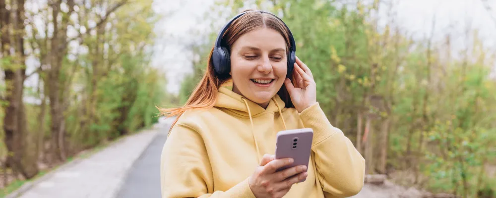 nainen, keltainen huppari, kännykkä, kuulokkeet