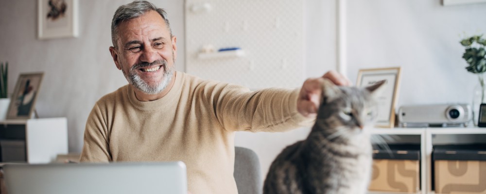 Harmaantunut mies pitää työstään tauon silittääkseen kissaa.