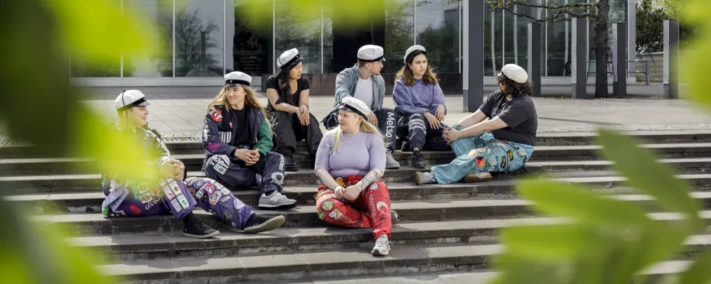 Opiskelijoita istumassa ulkona portaikossa, kesän vihreitä lehtiä etualalla.