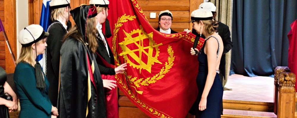 Juhla-asuisia ihmisiä teekkarilakit päässään lipun ympärillä.