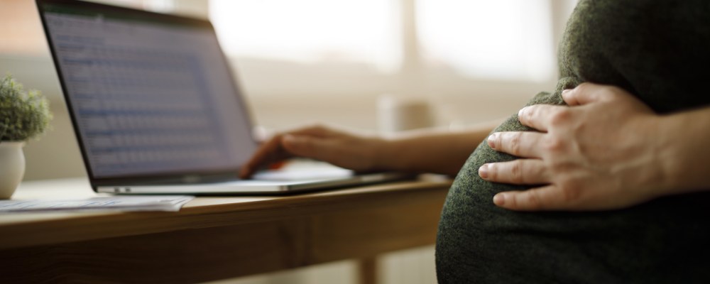 Raskaana oleva henkilö kannettavan tietokoneen ääressä.