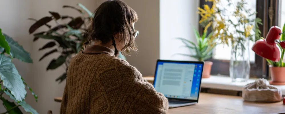 Nuorehko neisoletettu istuu tietokoneen ääressä kotonaan.