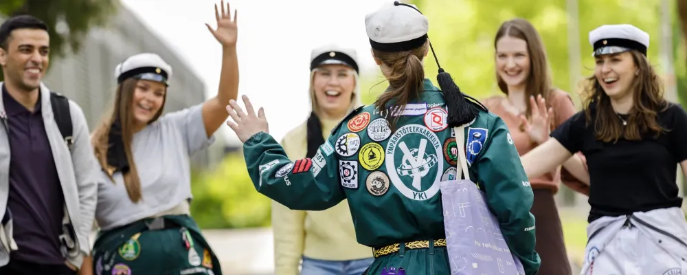 Joukko opiskelijoita tervehtii iloisesti toisiaan.