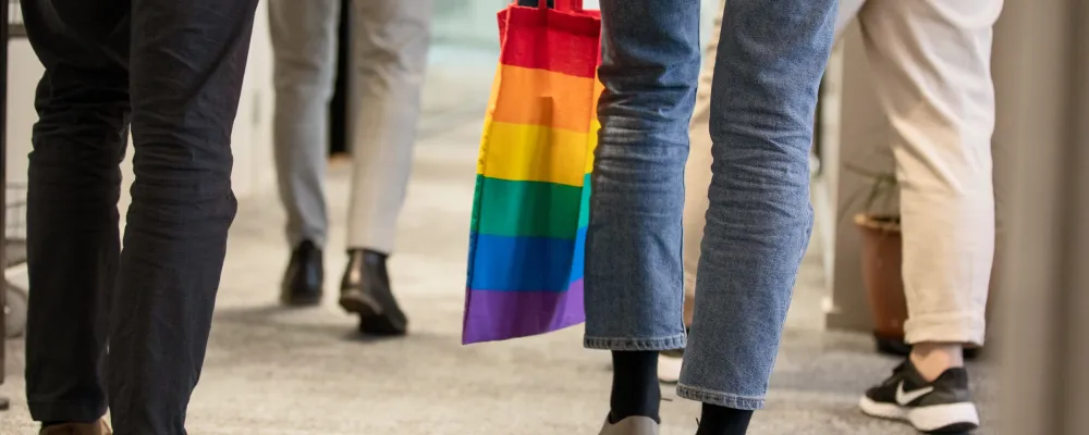 Kävelevien ihmisten jalkoja ja sateenkaaren värinen kassi.