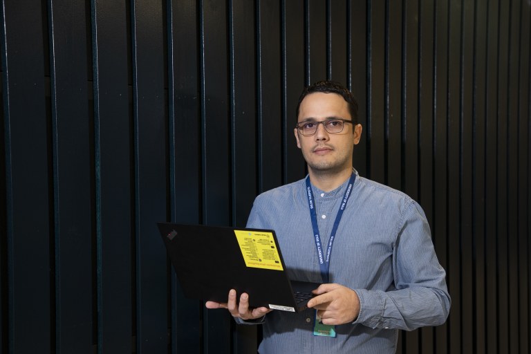 TEKin väitöskirjapalkittu, apulaisprofessori Onel Luis Alcazar López seisoo tummaa seinää vasten ja pitää kannettavaa tietokonetta kädessään.