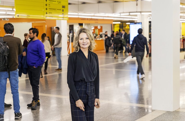 Sanna Tuomela seisoo Oulun yliopiston käytävällä, taustalla yliopiston väkeä.