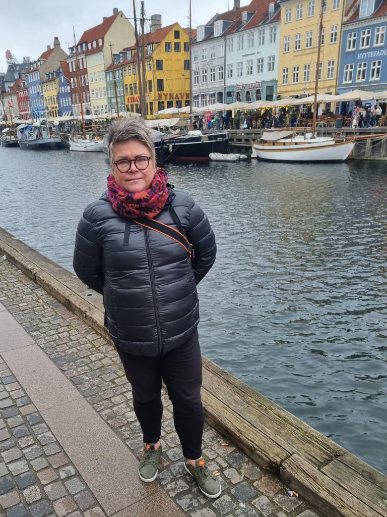 Anne Soikkeli seisoo kadulla, takanaan Nyhavnin värikkäät talot.