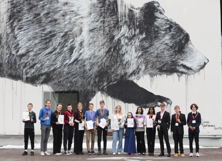 Winners of the TuKoKe 2023 Competition, behind them a wall painting of a bear.